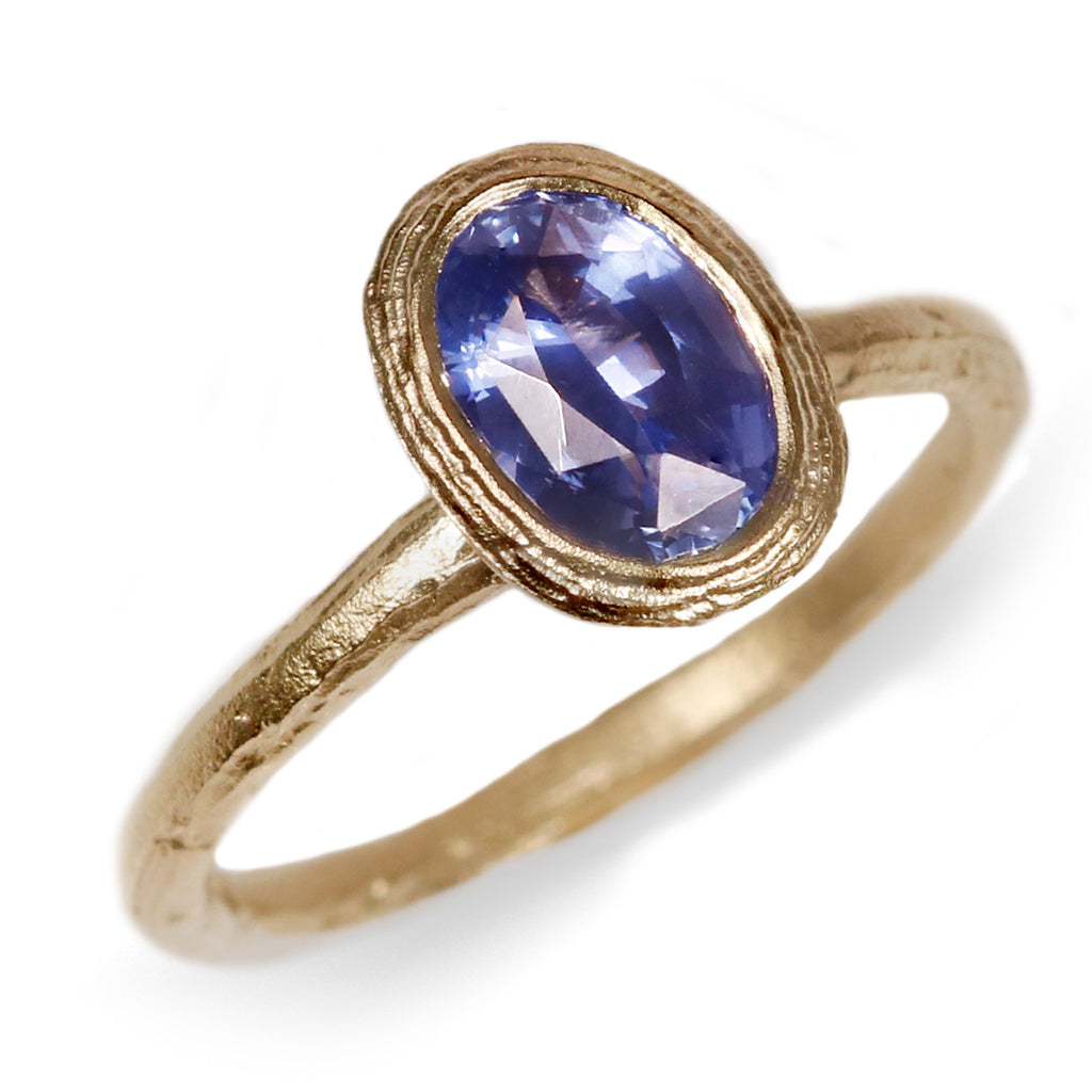 oval blue sapphire and textured yellow gold ring on a white background 