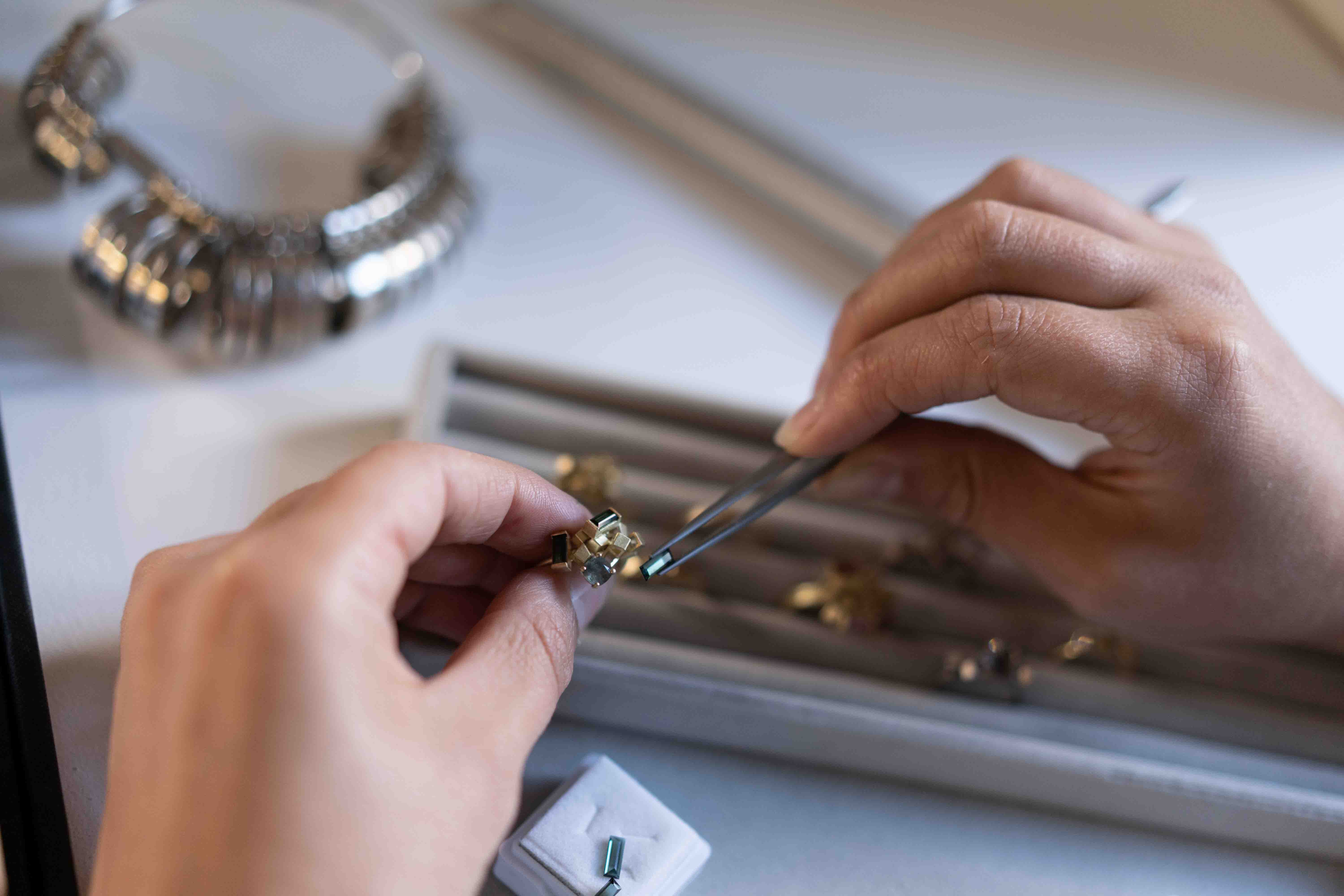 Alma Sophia, trying out different ring compositions in hewellery studio with gold rings and jewellery tools in the background