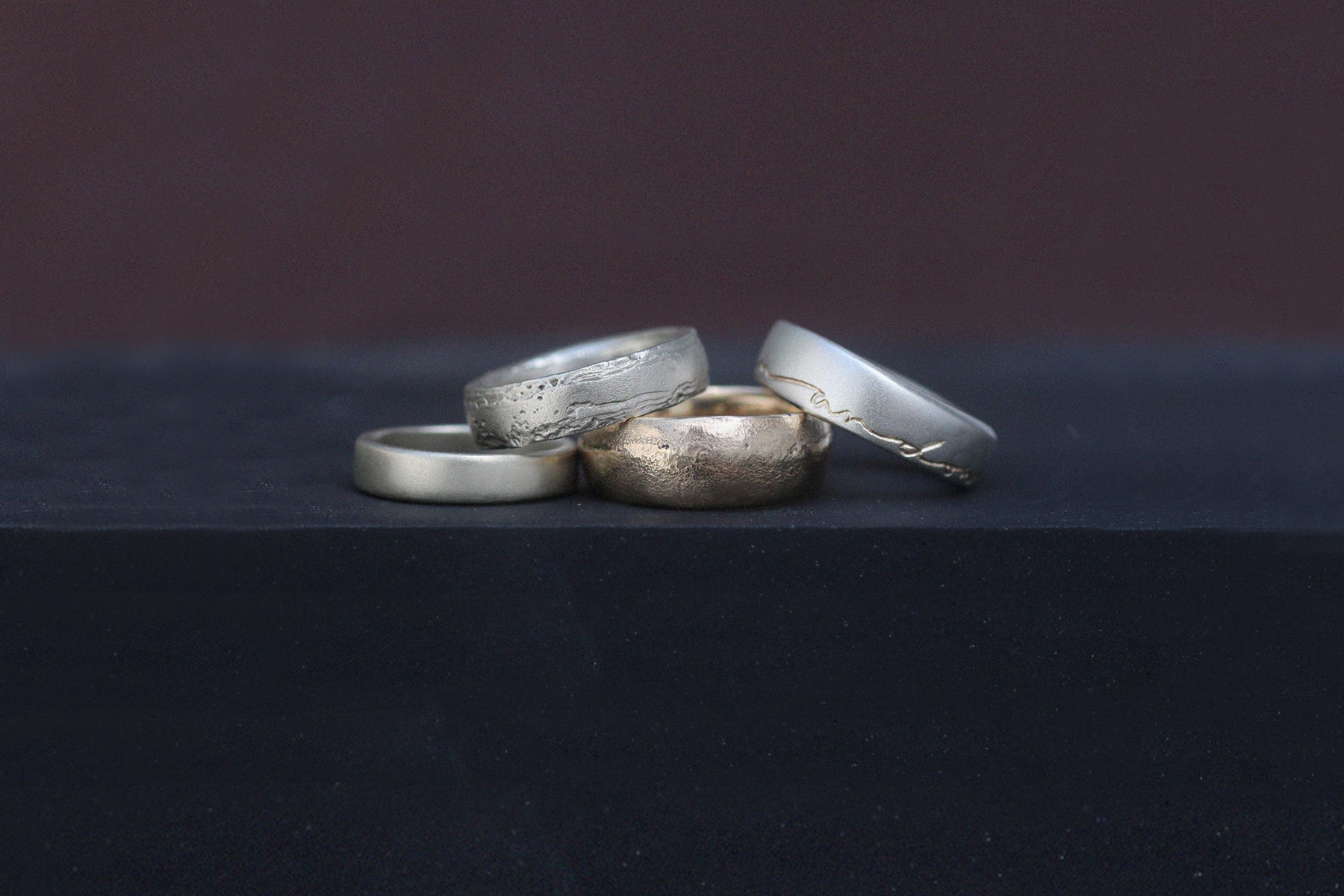 Modern mens wedding band rings shown in rose gold, white gold and yellow gold displayed on a concrete block.
