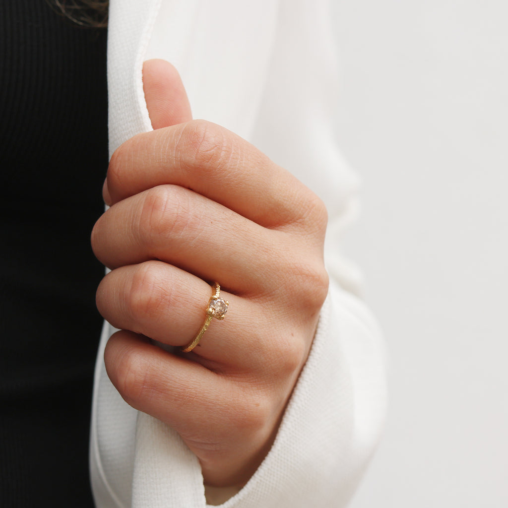 Close-up of a hand wearing a gold ring with a champagne diamond on a blurred background