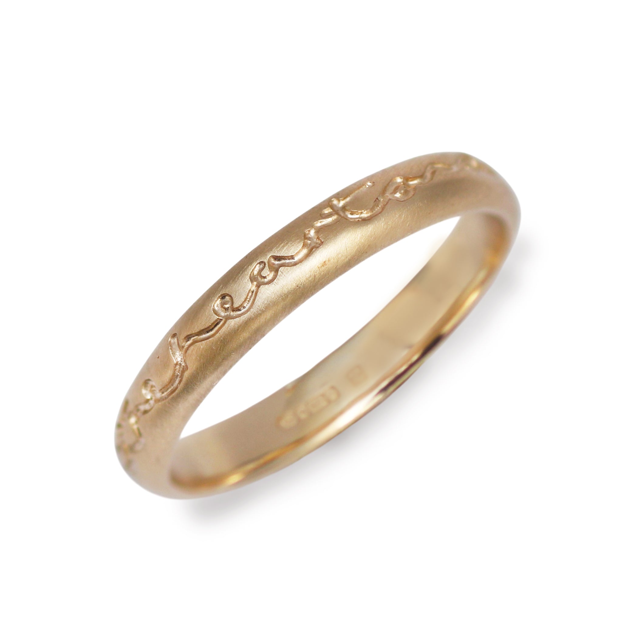An etched yellow gold slim ring etched with the words 'heart and mind they meet' on a white background. 