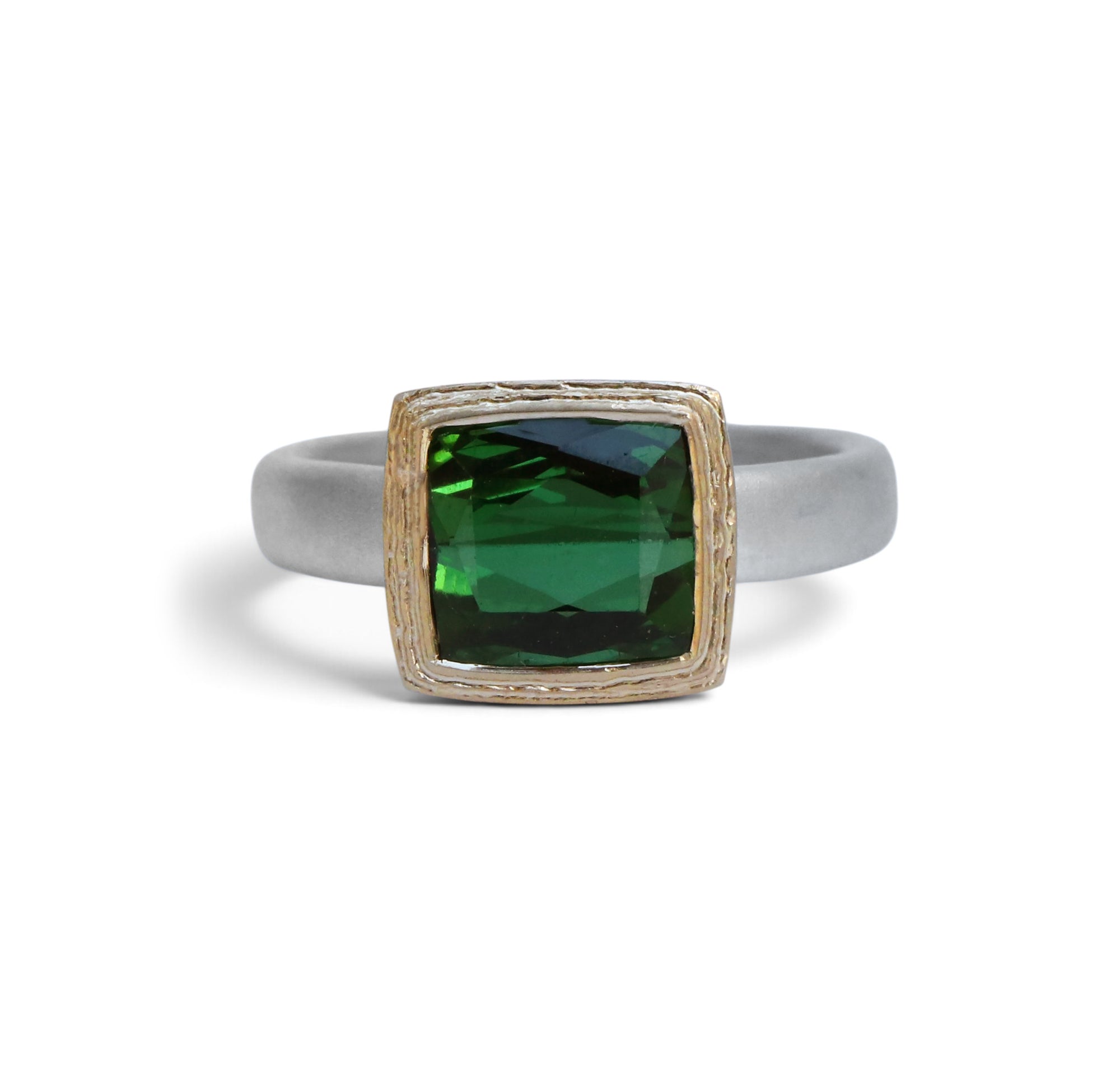 A square bezel-set ring featuring a faceted green gemstone in a textured gold-toned frame, mounted on a matte silver-toned band, shown against a plain white background.