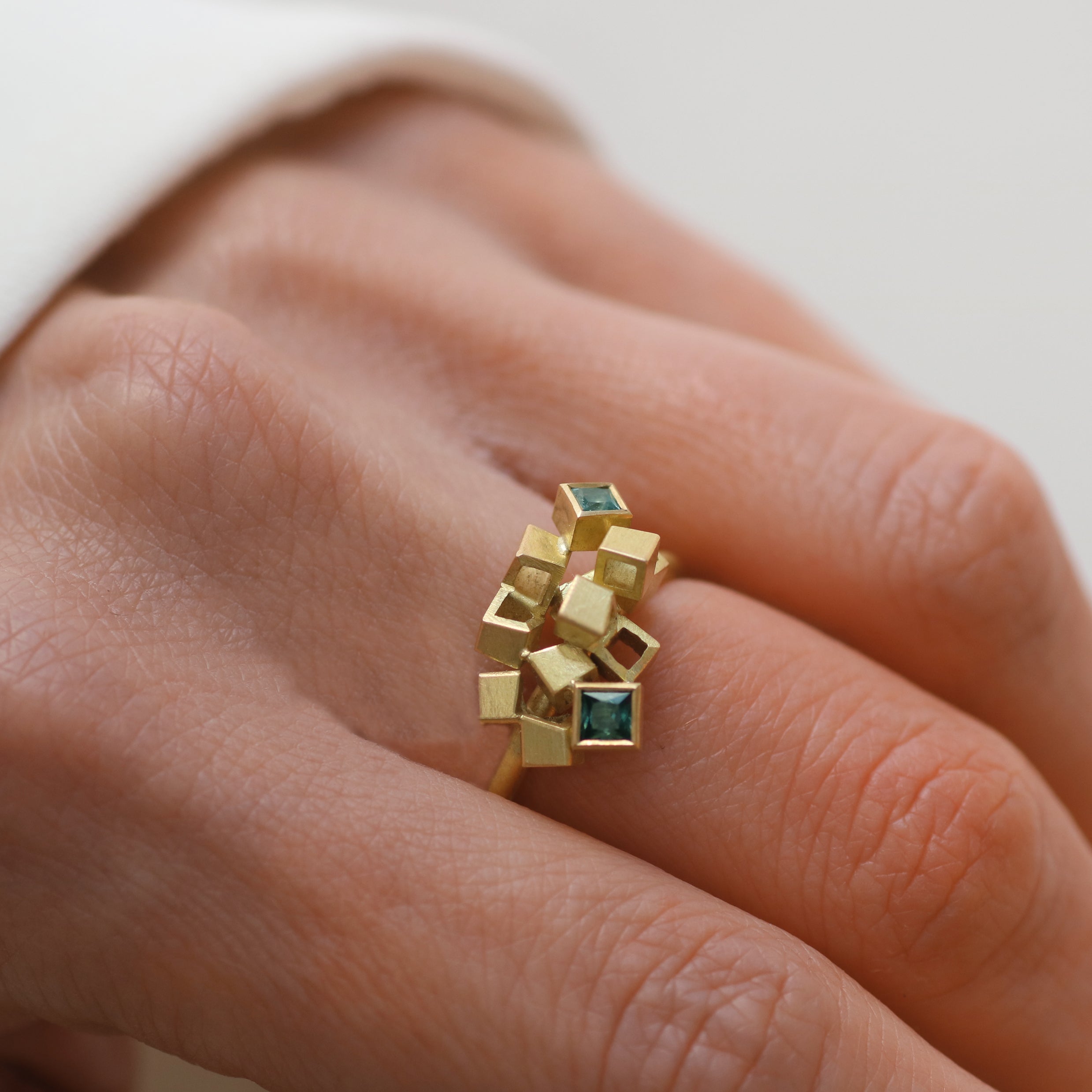 Gold Cube Detail ring with blue square stones worn on hand pale background