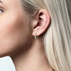 A close-up side profile of a woman with blonde hair wearing a small silver bird claw hoop earring.