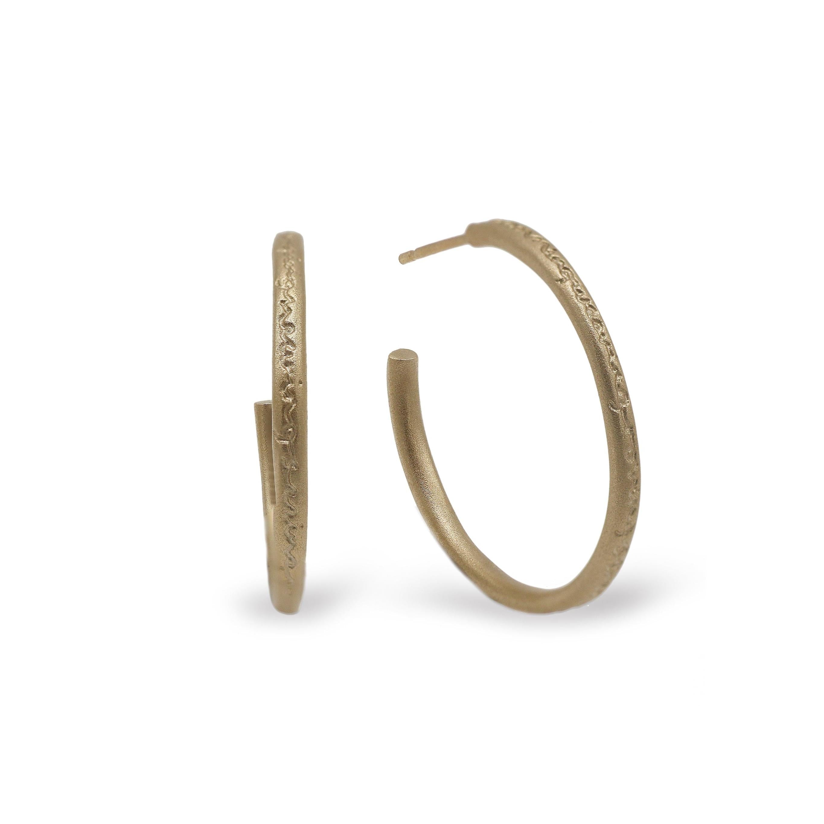 yellow gold hoop earrings with words etched on a white background