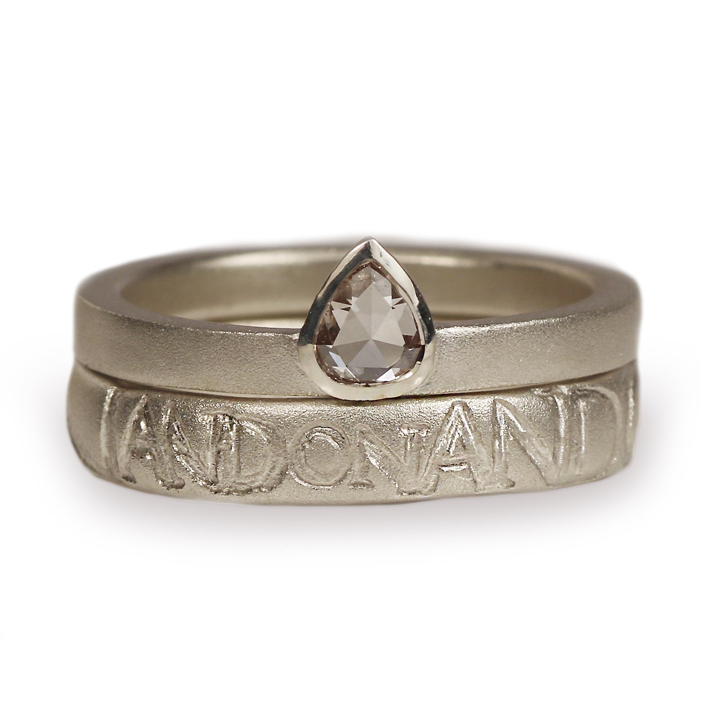 A white gold ring set featuring a textured band engraved with the name 'on and on' and a smooth band with a faceted teardrop-shaped clear gemstone, shown on a white background.