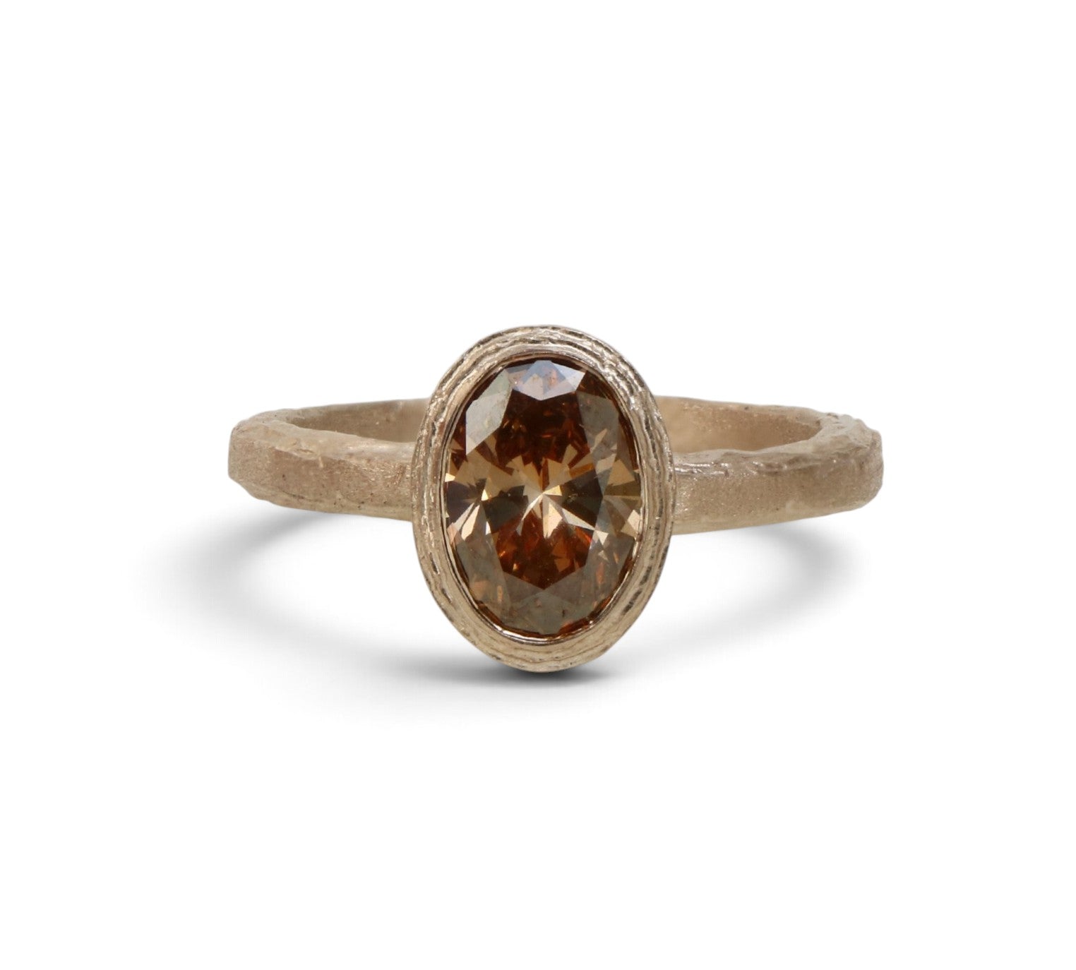 A rustic gold ring featuring an oval-cut brown gemstone in a textured bezel setting, shown on a clean white background.