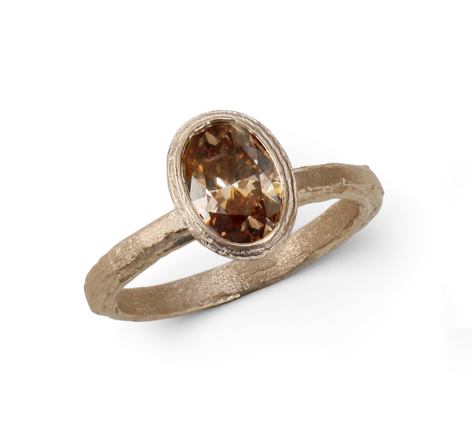 A textured gold ring featuring an oval-cut brown lab grown diamond in a bezel setting, shown on a clean white background.