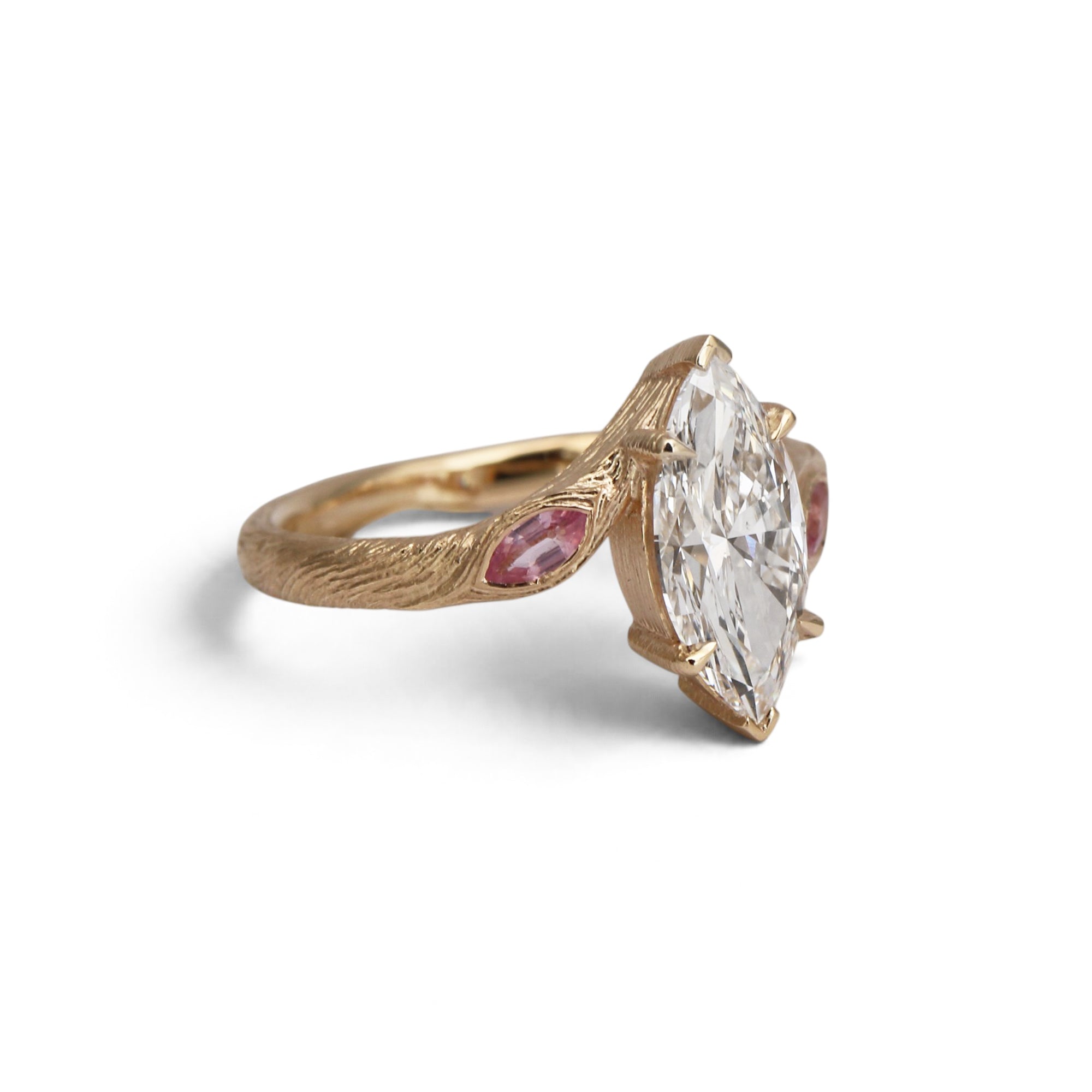 A gold ring featuring a large marquise-cut clear gemstone in a prong setting, accented by two small round pink gemstones on either side of the band, shown on a white background.