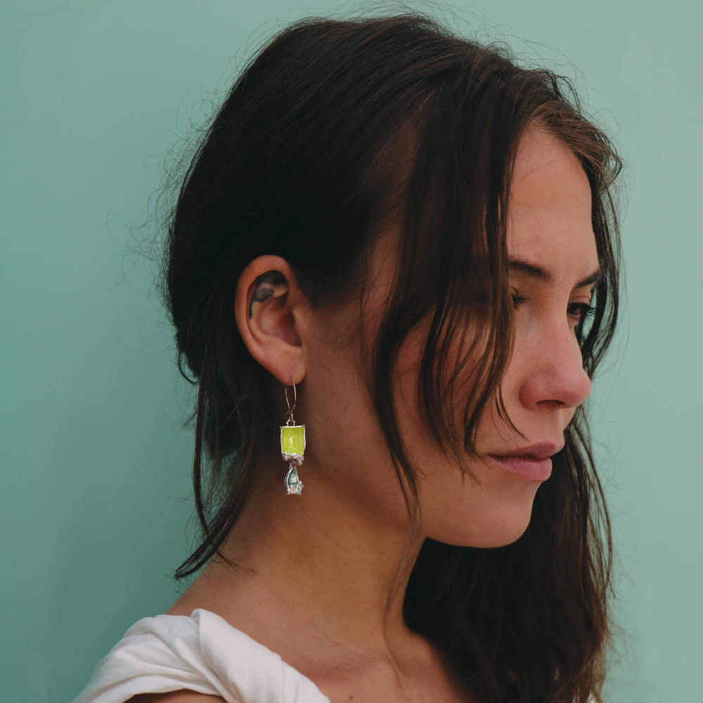 Woman wearing a green earring against a teal background