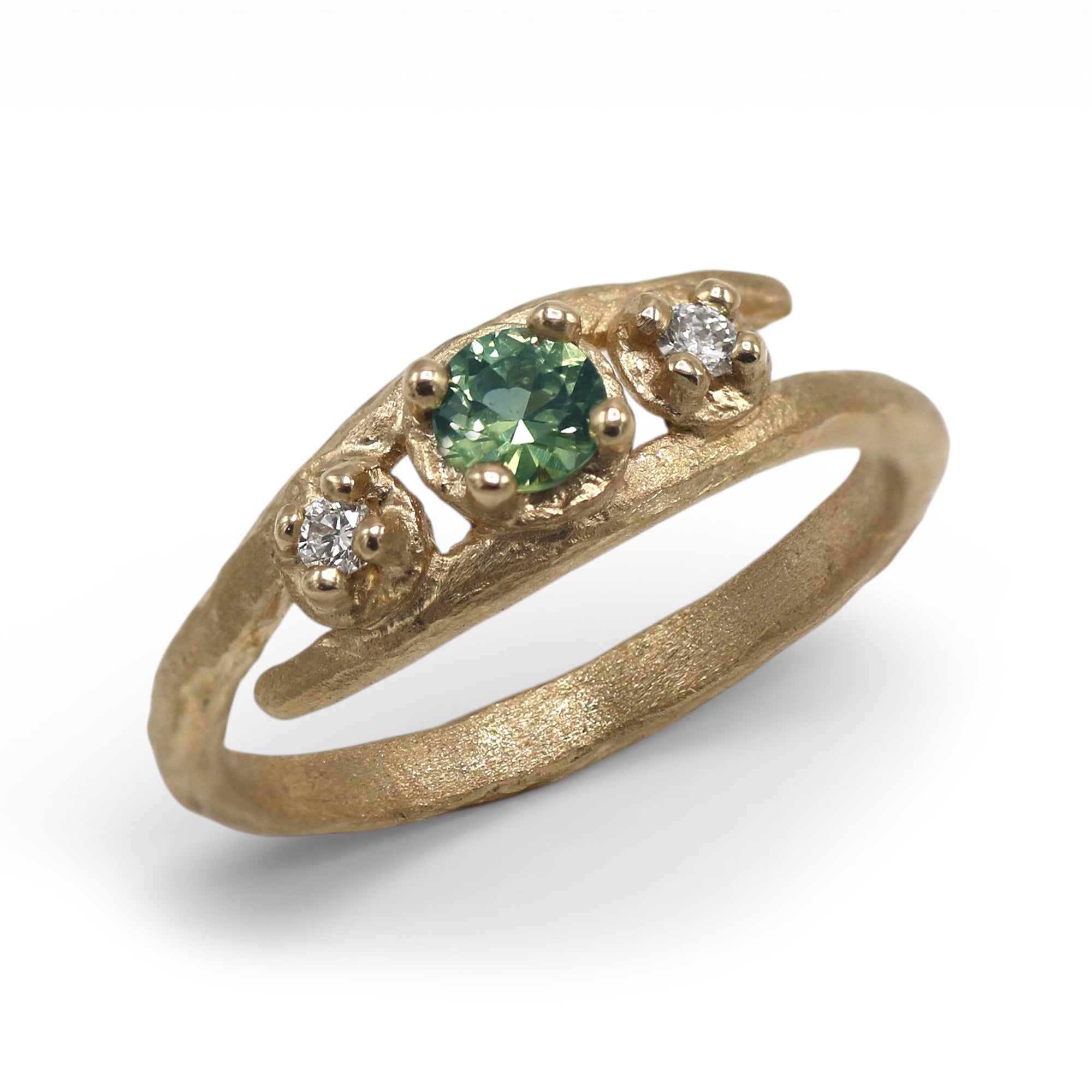 A textured yellow gold ring featuring a central round green gemstone flanked by two small clear accent stones, set against a clean white background.