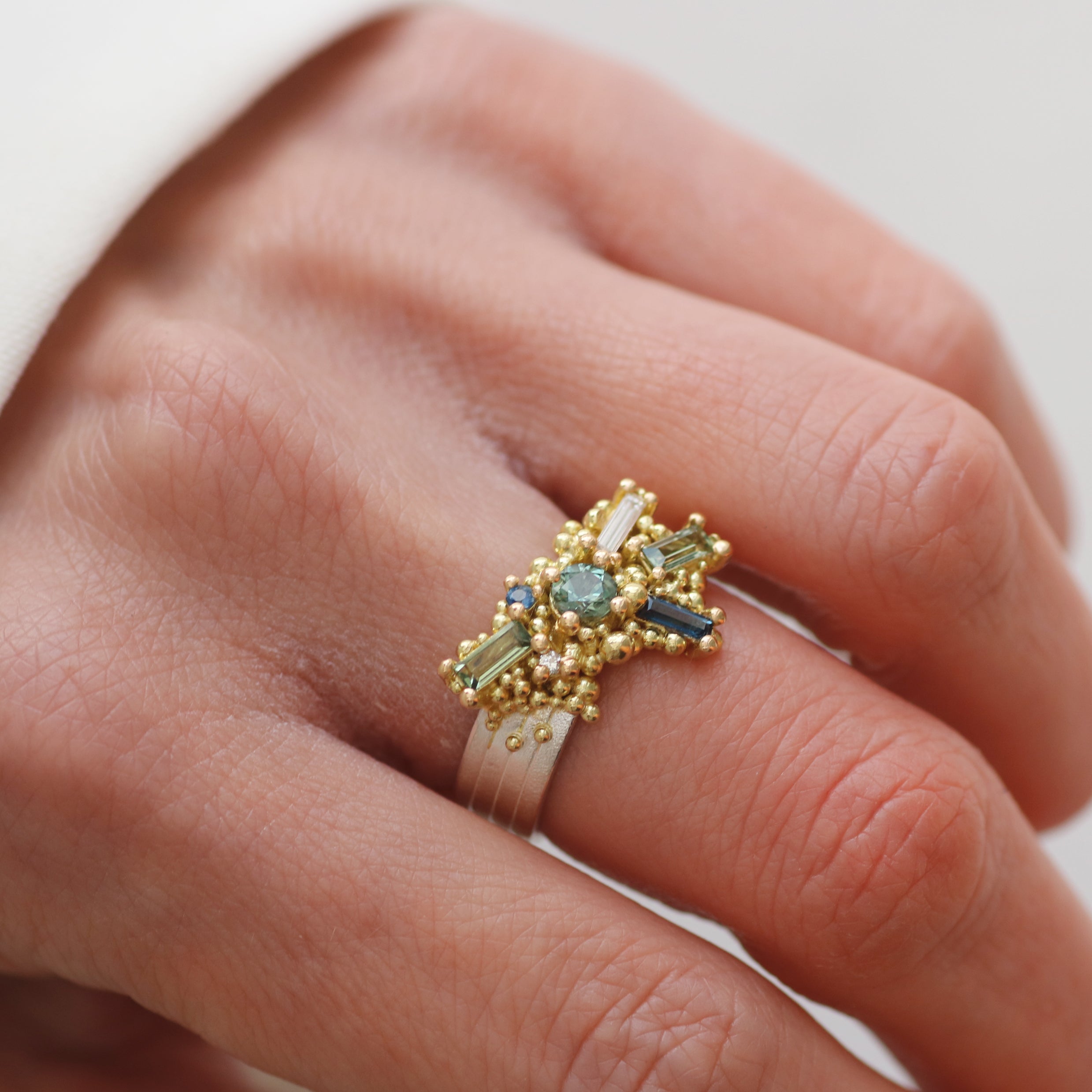 Gold ring with green gemstones on a person's finger against a neutral background