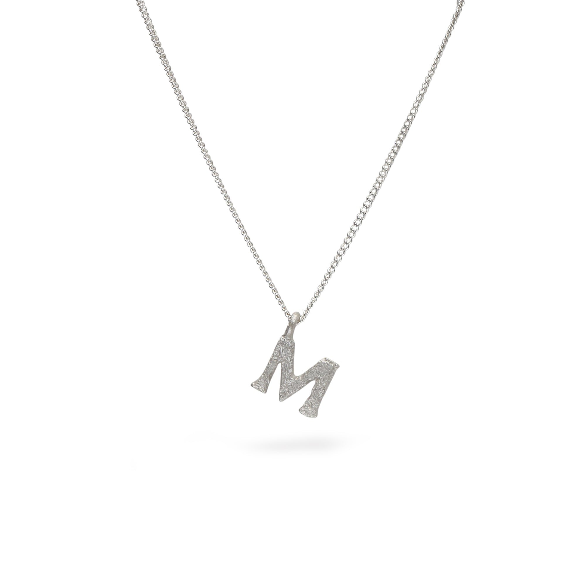A silver initial necklace featuring a textured capital letter 'M' pendant on a delicate silver chain, shown against a plain white background.