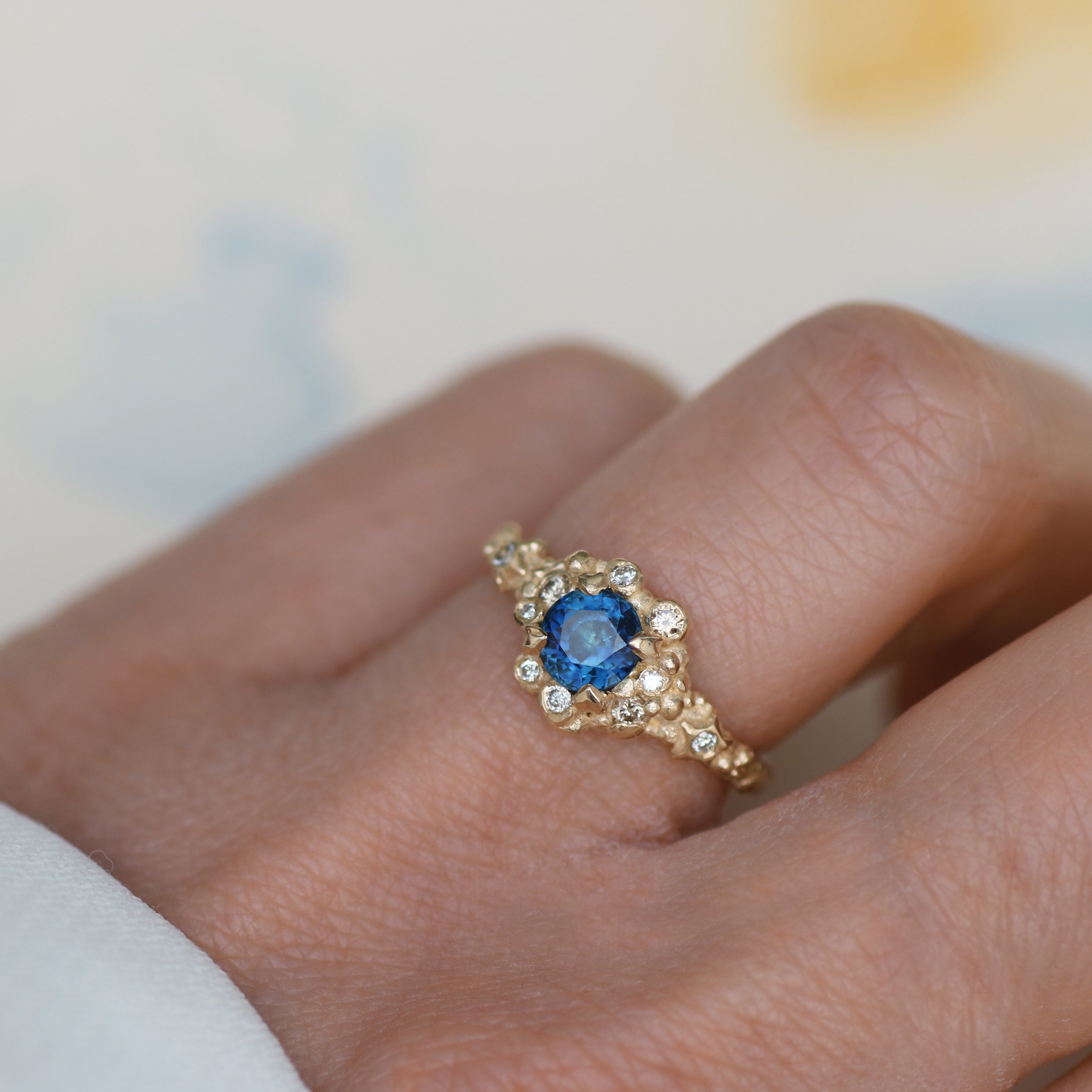 blue sapphire yellow gold diamond ring worn on a neutral background
