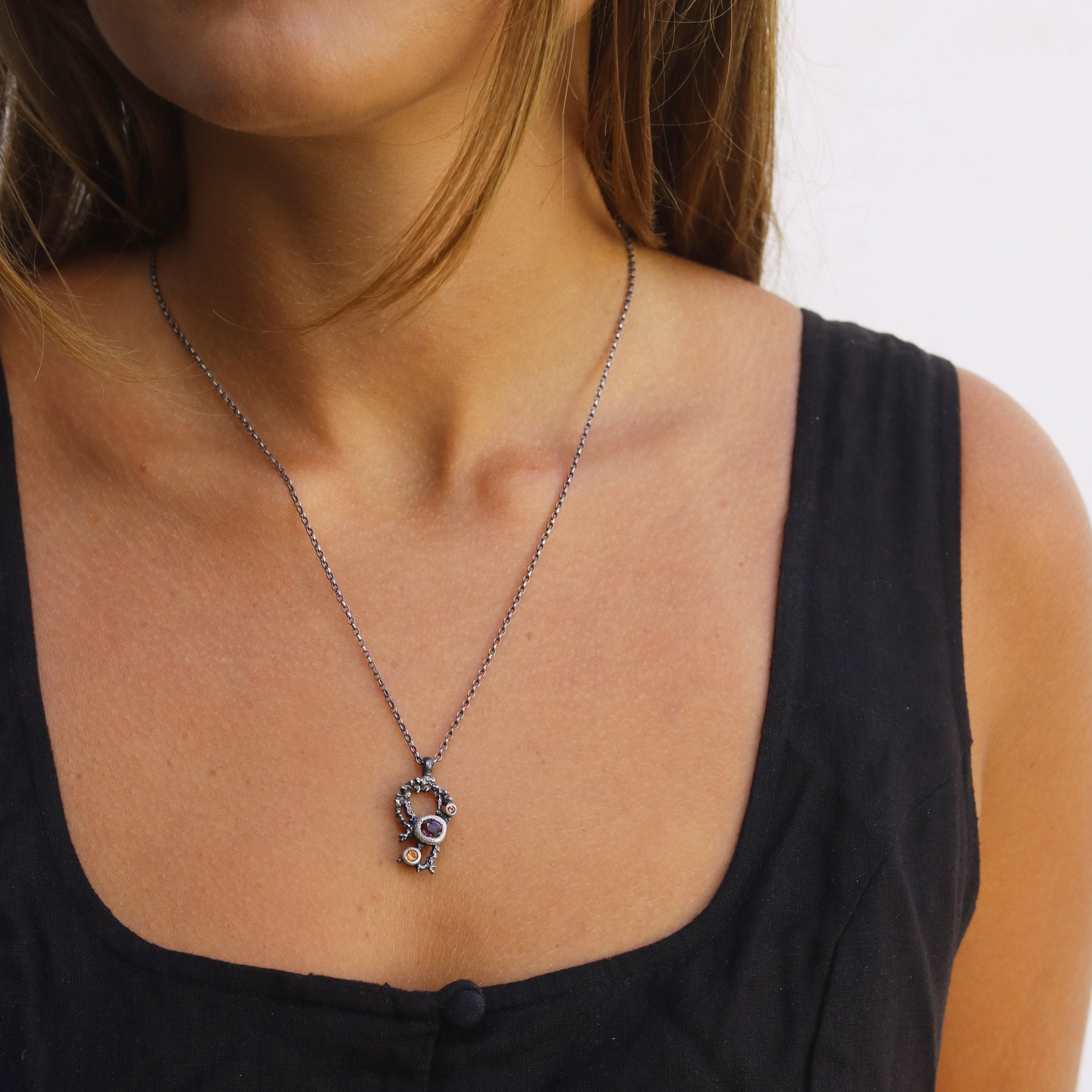 Close-up of a woman wearing a black top with a necklace featuring a purple spinel