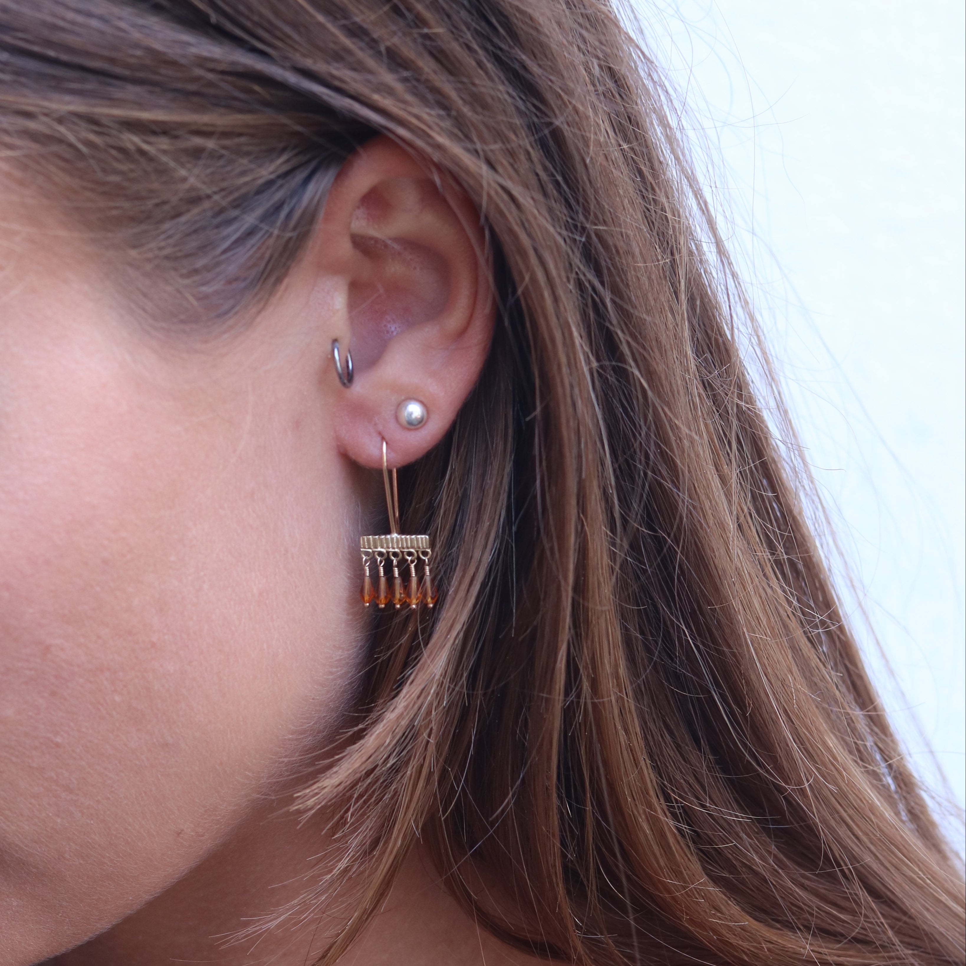 Close-up of a person wearing a gold earring with Citrine drops.