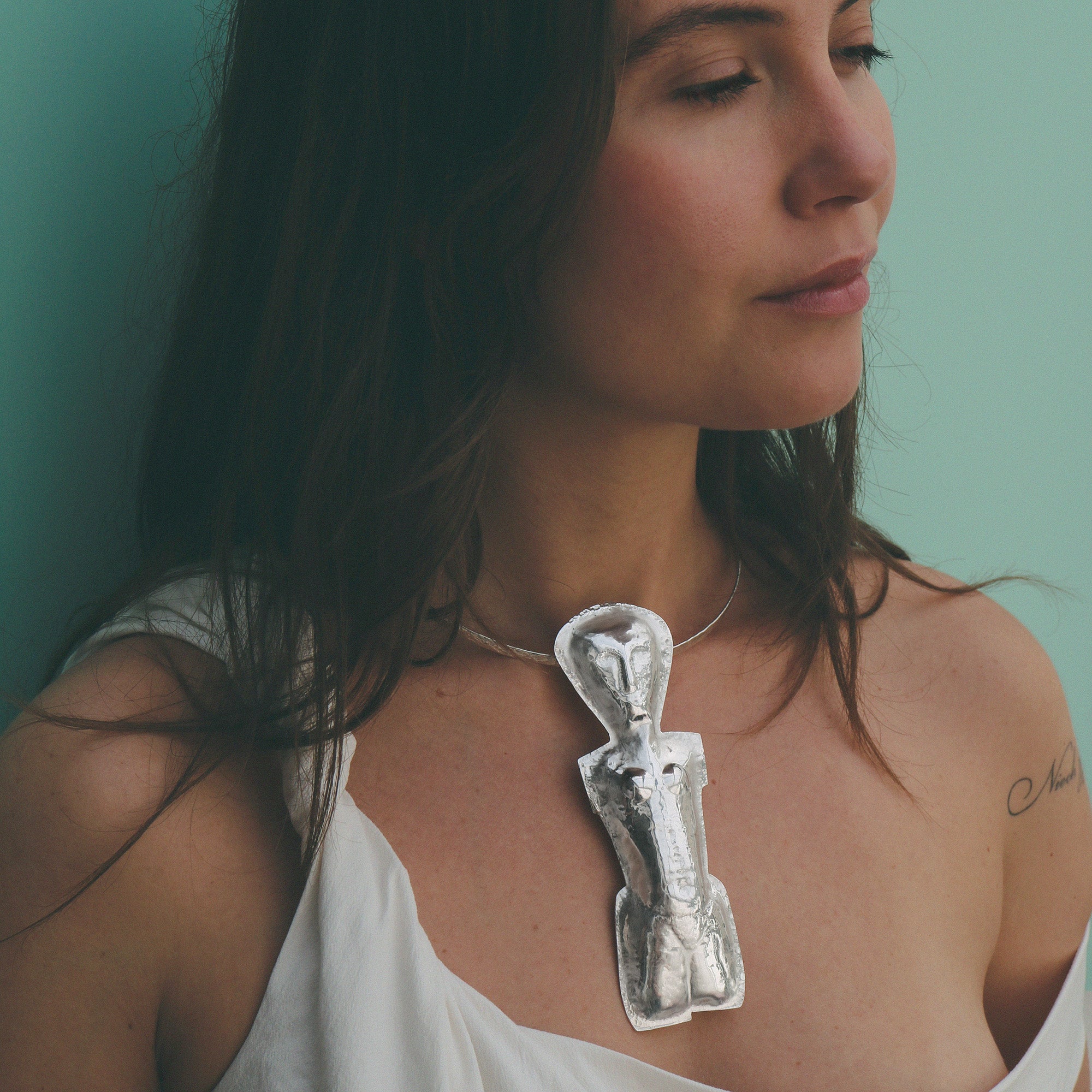 Woman wearing a unique necklace with a silver pendant against a teal background