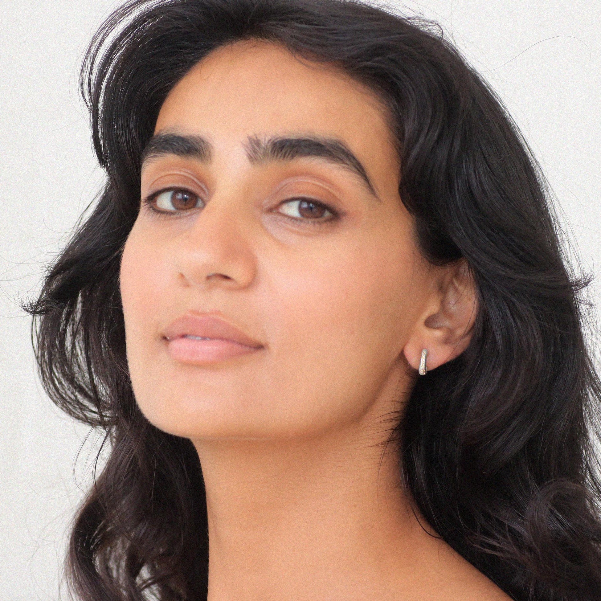 Close-up of a person with dark hair and earrings against a light background
