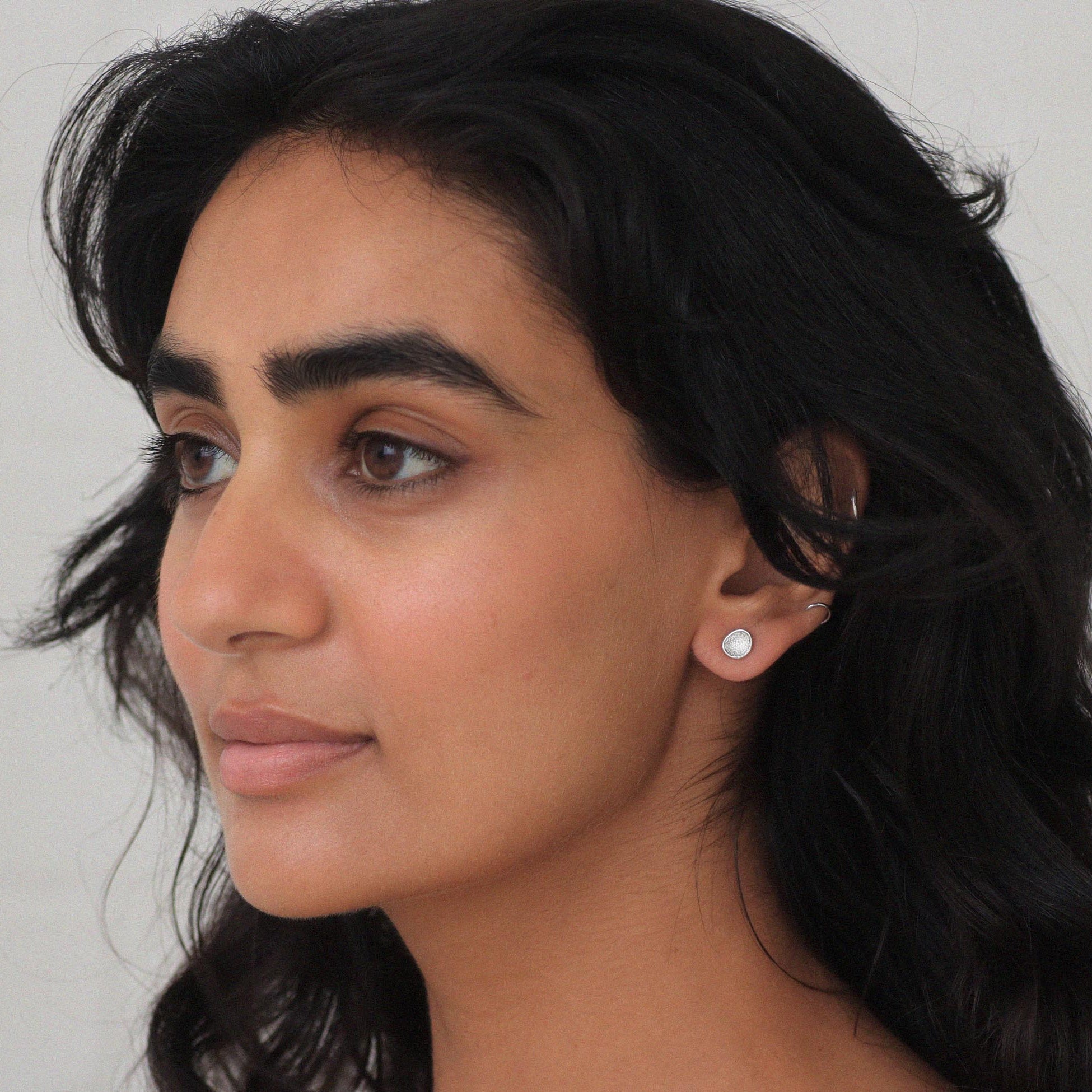 Close-up of a woman wearing silver textured earrings against a neutral background
