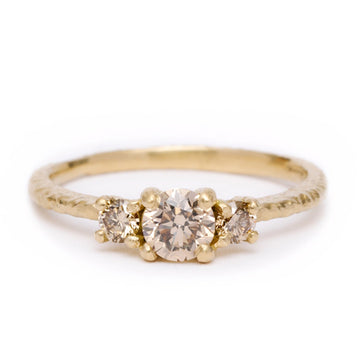 An 18ct yellow gold ring with three champagne diamonds, the central diamond is the largest and placed in the front, with two smaller ones on either side. The band has a textured finish.