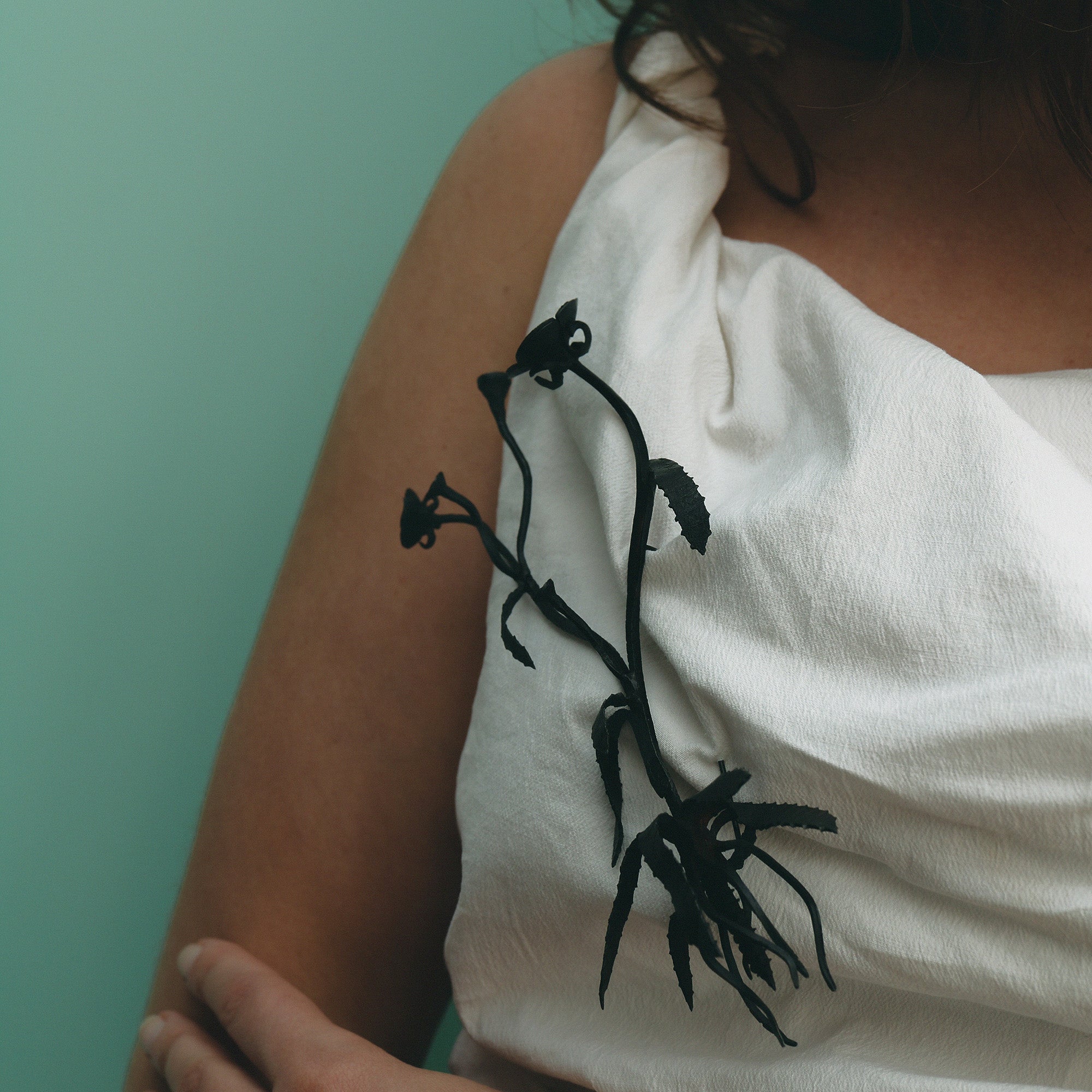 Person wearing a white garment with black floral brooch against a light green background