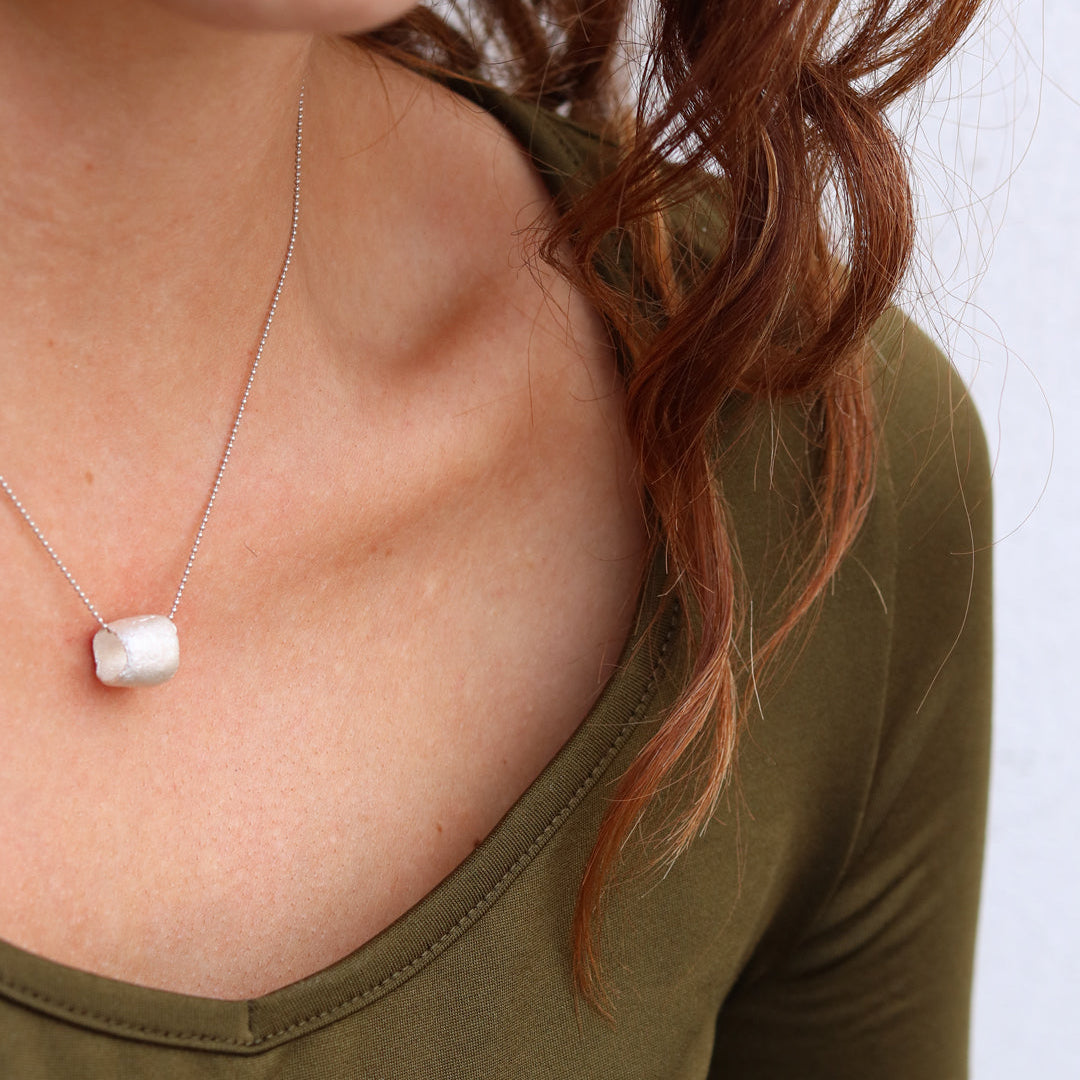 Necklace with a pendant worn by a person in an olive green top against a white background
