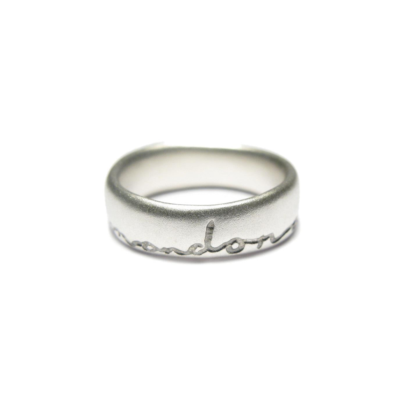 Silver wedding ring with 'and on' etched in black. Displayed on a white background