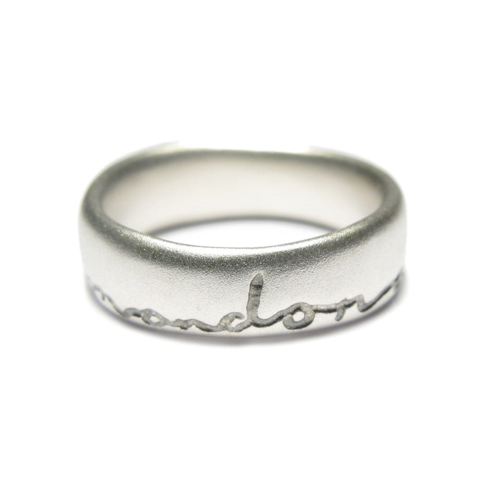 Silver wedding ring with 'and on' etched in black. Displayed on a white background