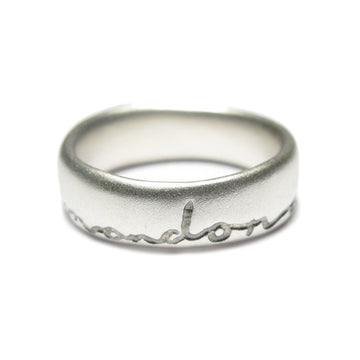 Silver wedding ring with 'and on' etched in black. Displayed on a white background
