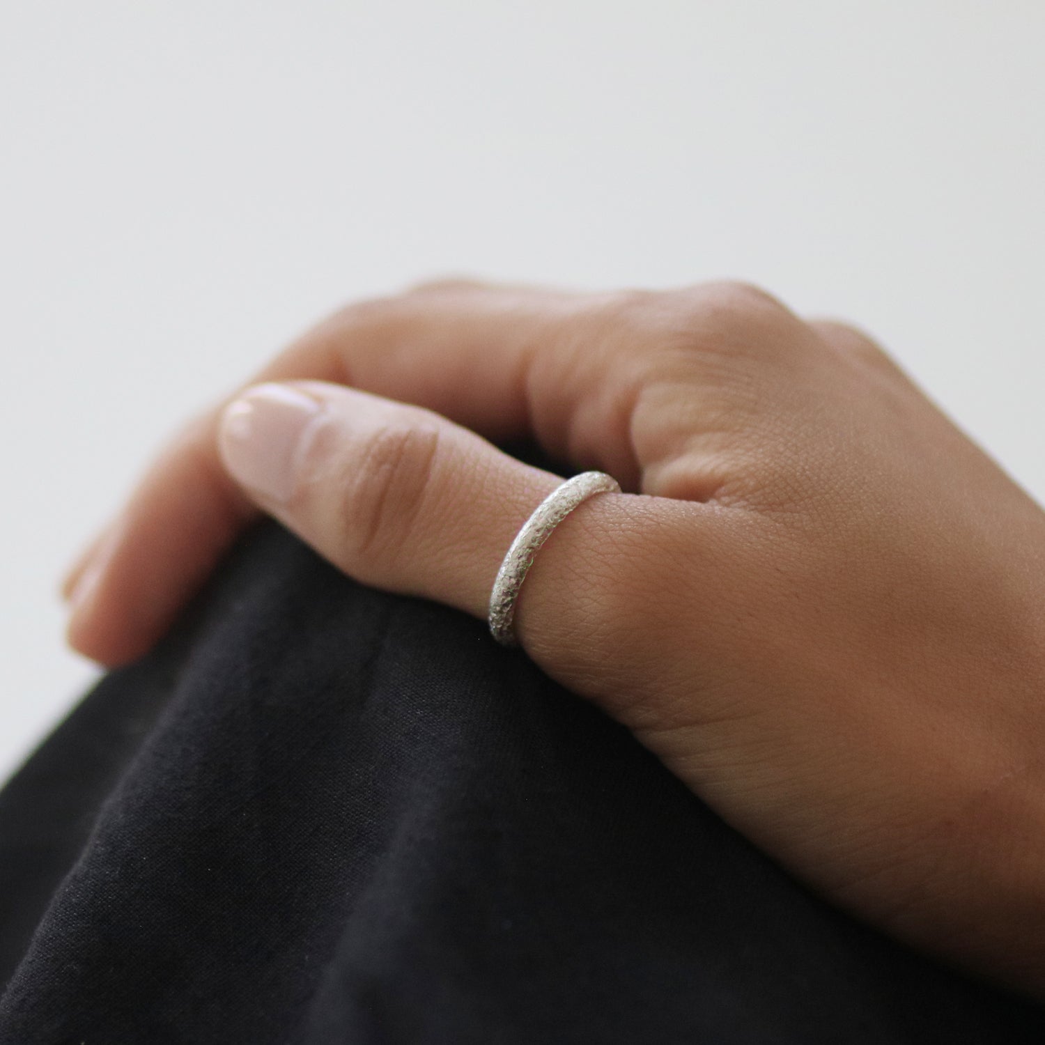 Close-up of a hand wearing a silver ring on a plain background