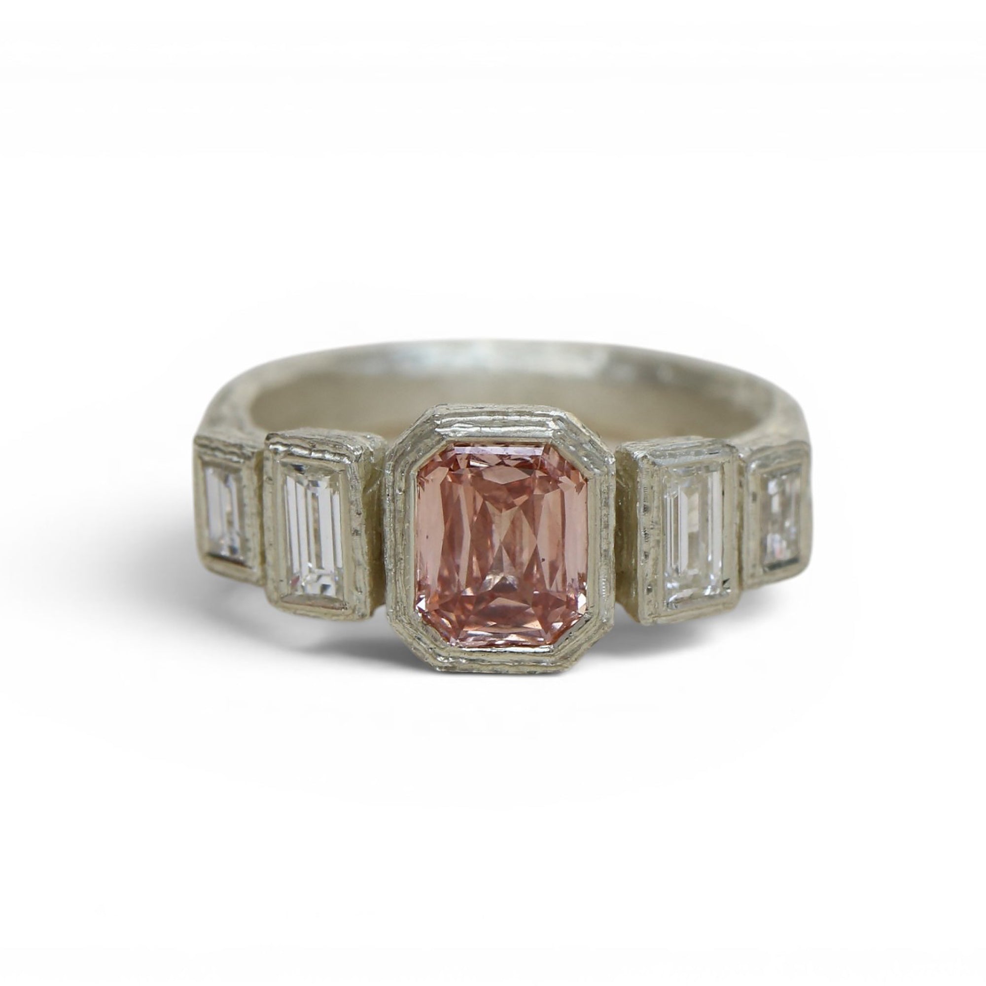 A vintage-style silver ring featuring a central rectangular pink gemstone flanked by smaller clear baguette and round-cut stones, set against a plain white background.