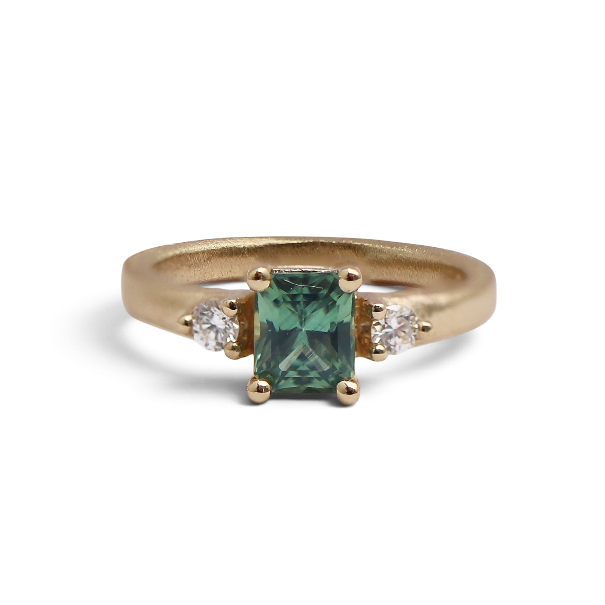 A yellow gold ring featuring a rectangular emerald-cut green gemstone in the center, flanked by two small white diamond stones on a white background.