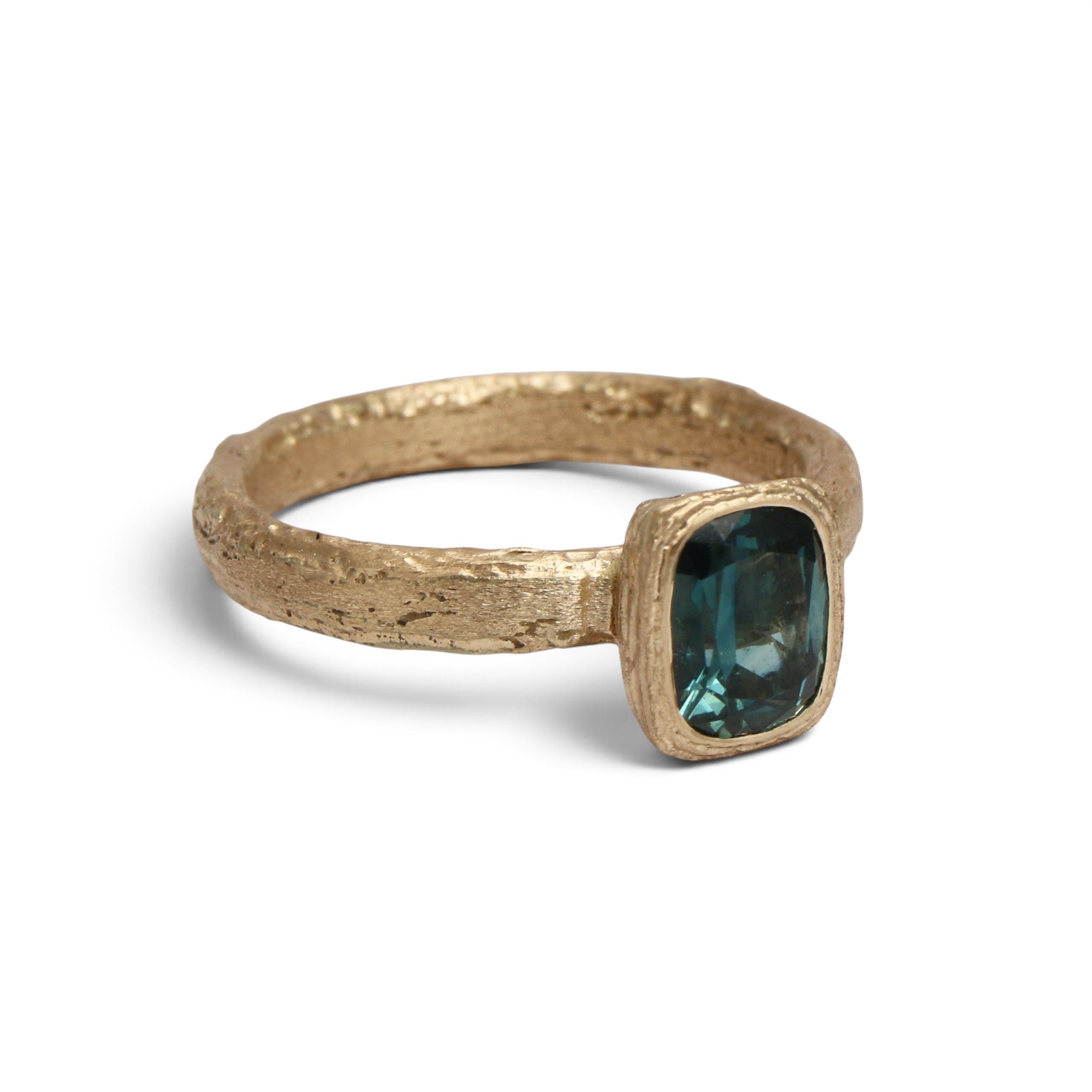 A textured gold ring featuring a emerlad cut dark teal gemstone, shown on a clean white background with a soft shadow.