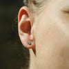 Close-up of an ear with a sapphire stud earring against a blurred background