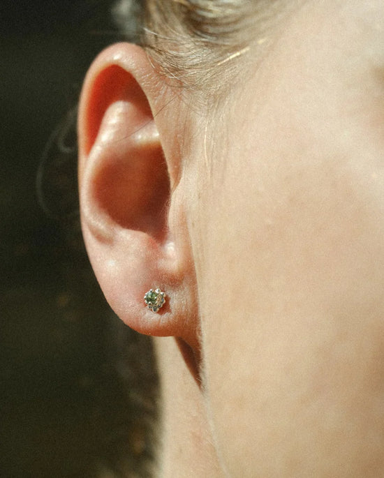 Close-up of an ear with a sapphire stud earring against a blurred background
