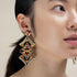 Close-up of a woman wearing gold and orange earrings against a neutral background