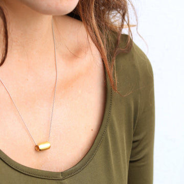 Person wearing a gold necklace with a small pendant on a plain background