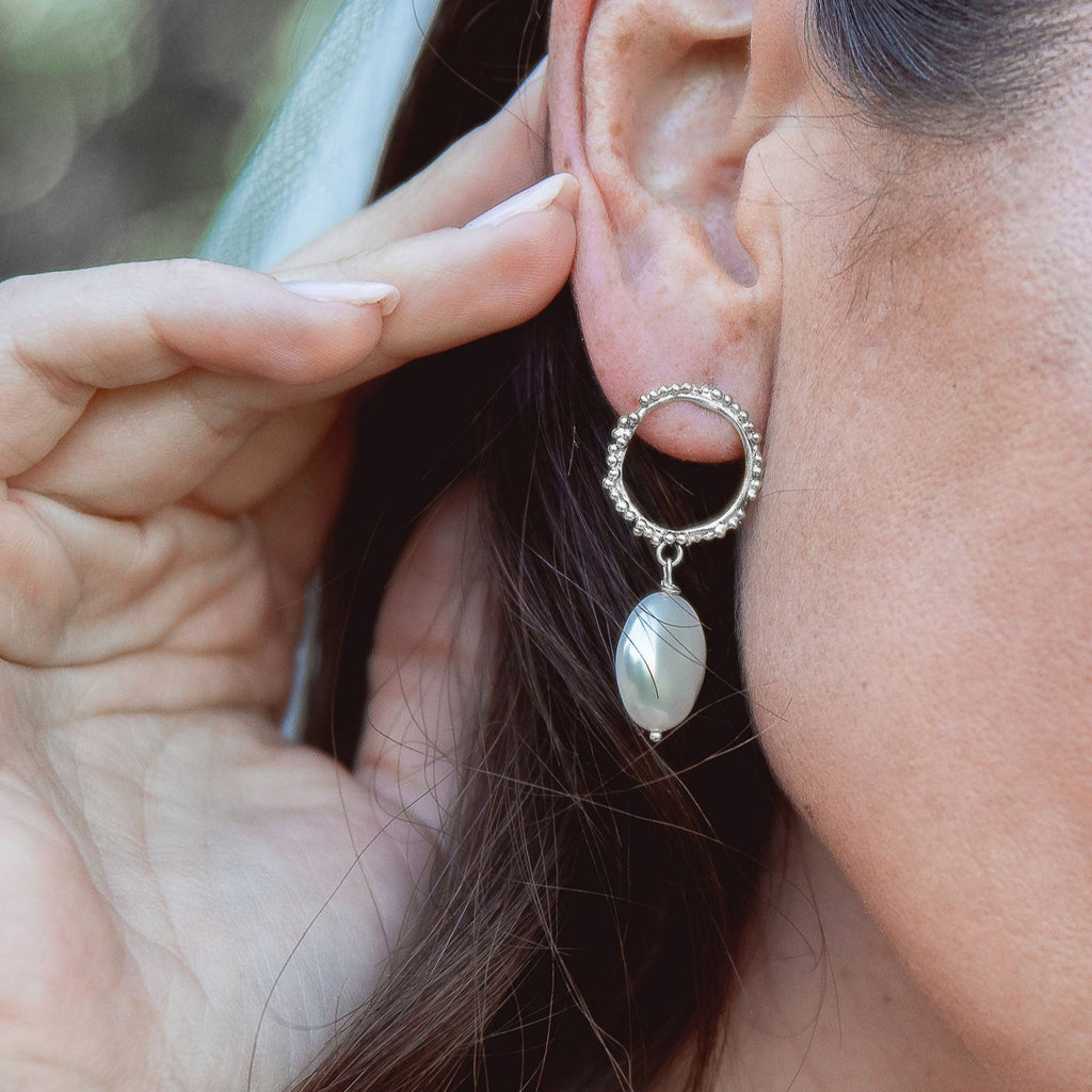 Close-up of a person wearing a hoop earring with a pearl-like bead.