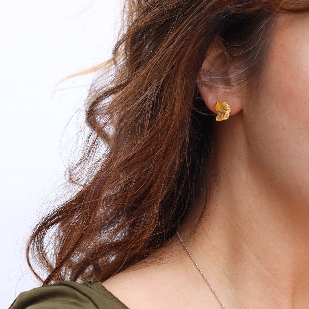 Close-up of a person wearing a gold earring with a plain background