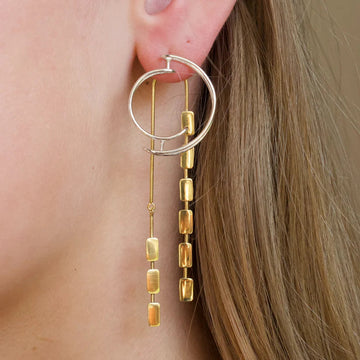 silver circle studs earrings with dangling gold bars worn by a person.