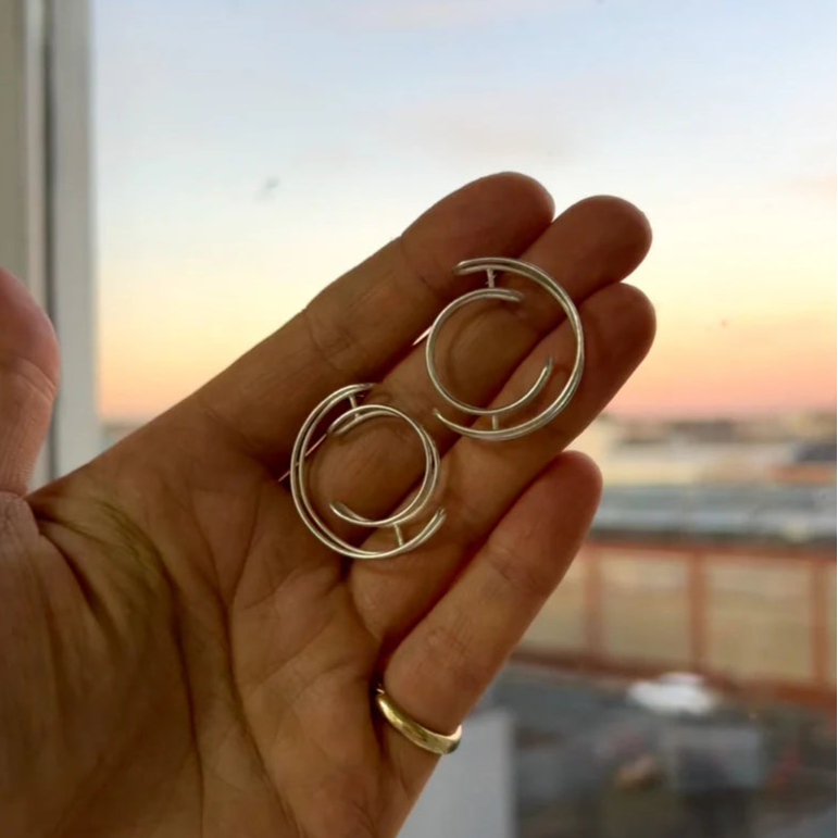 Hand holding a pair of silver hoop earrings with a blurred window background