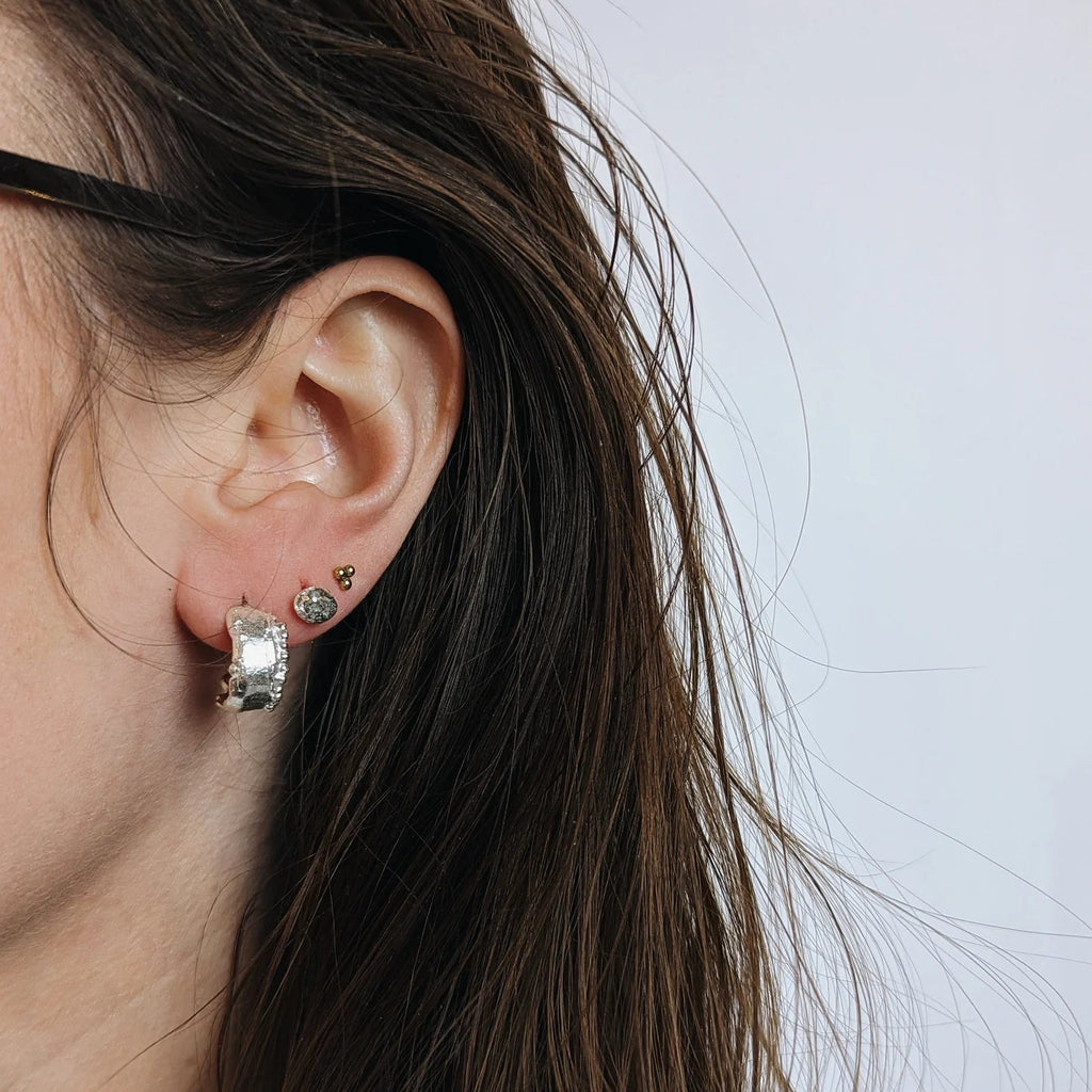 Close-up of a person wearing silver hoop earrings with a neutral background