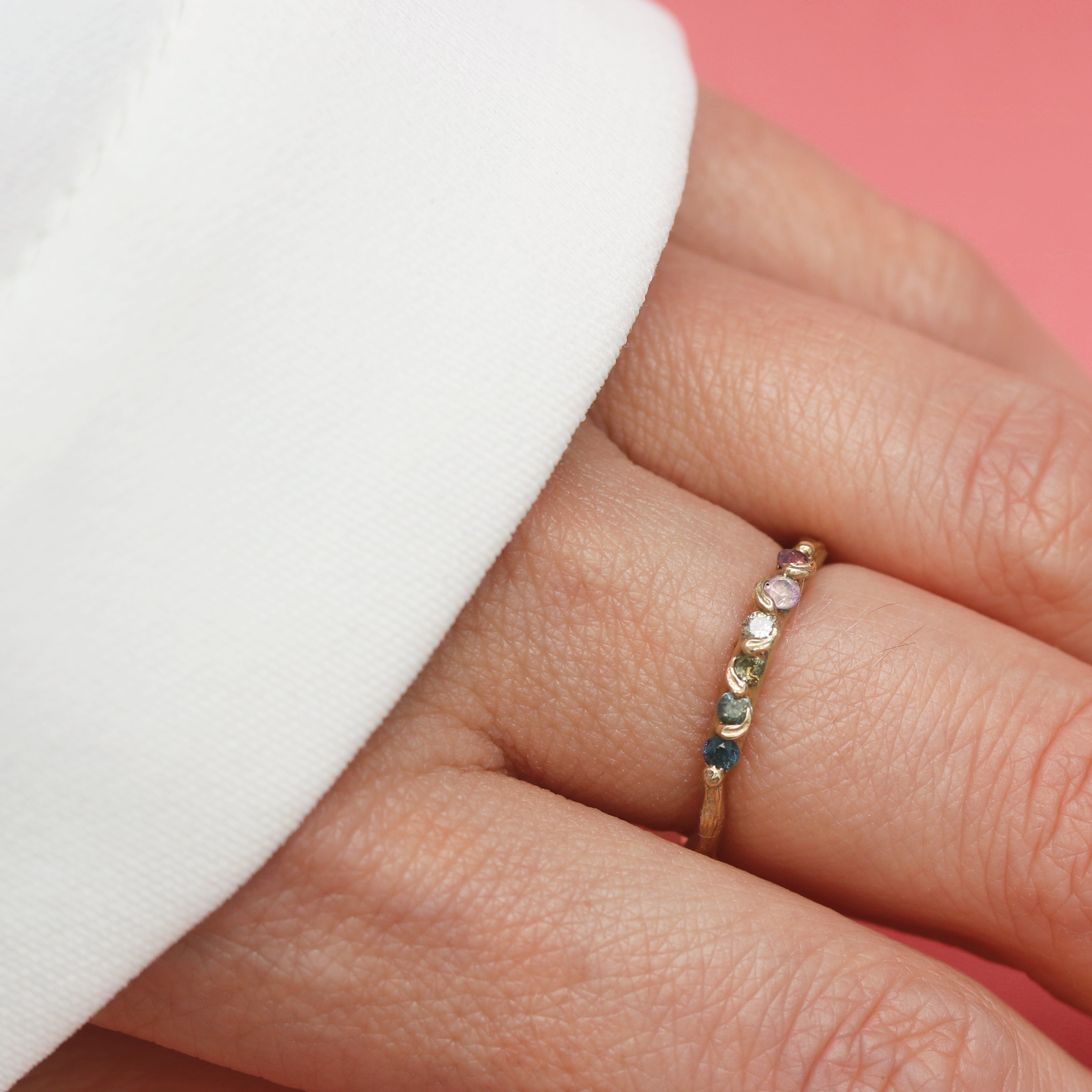 Close-up of a hand wearing a multicolored ring on a pink background