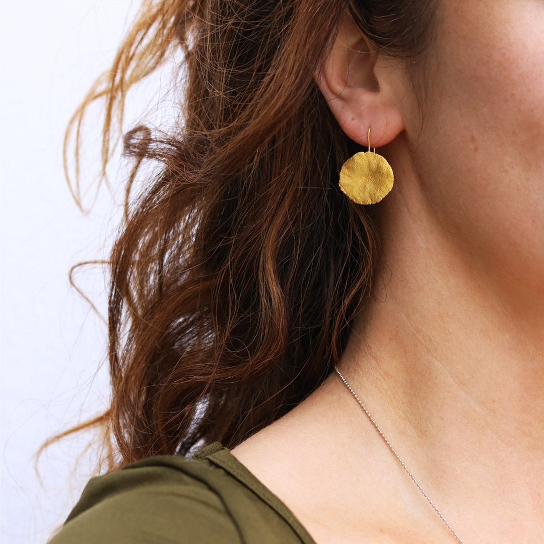 Gold earring worn by a person with a plain background