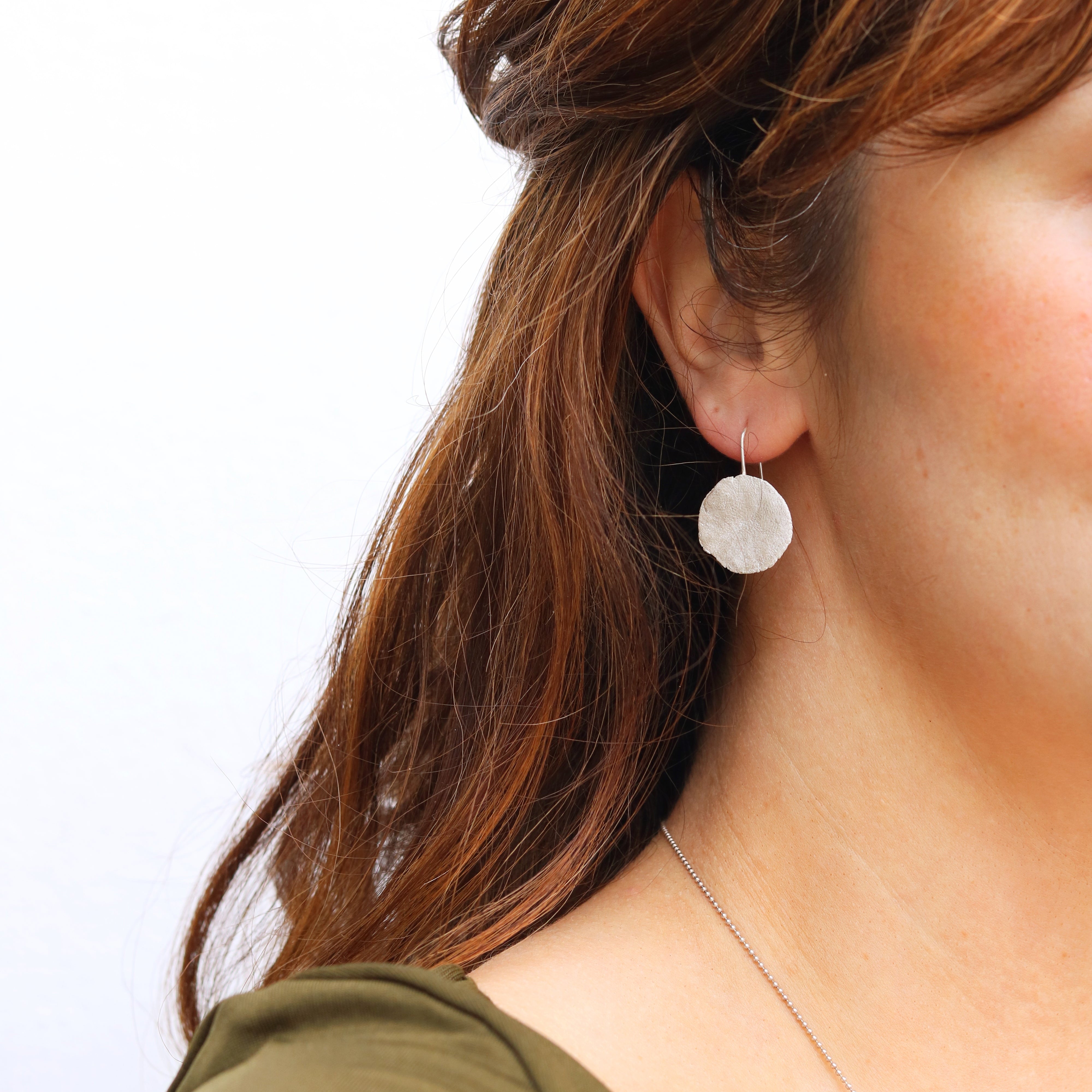 Close-up of a person wearing a round earring with a plain background