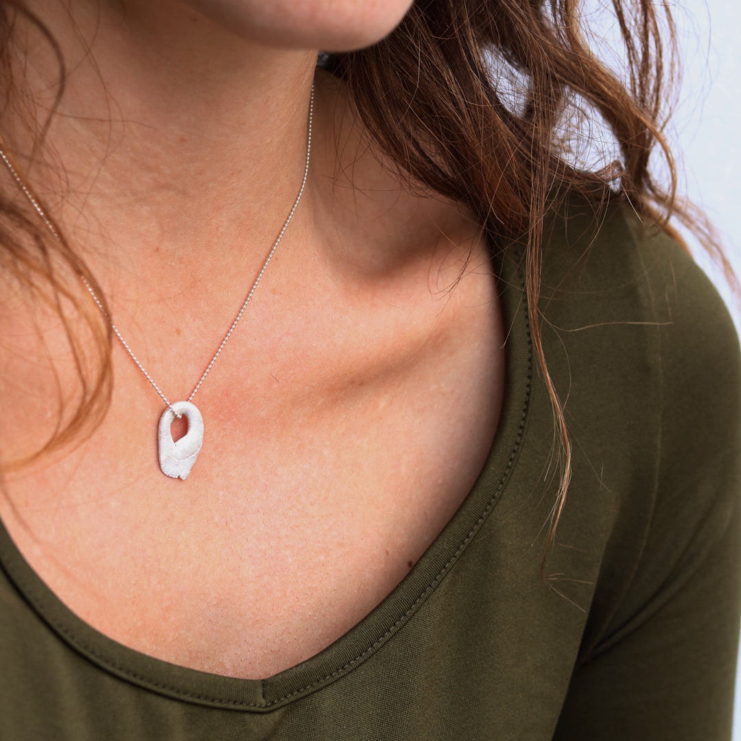 Person wearing a necklace with a unique silver pendant against a neutral background