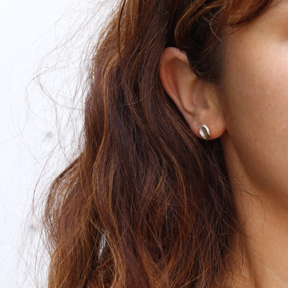 Close-up of an ear with a small silver earring against a neutral background