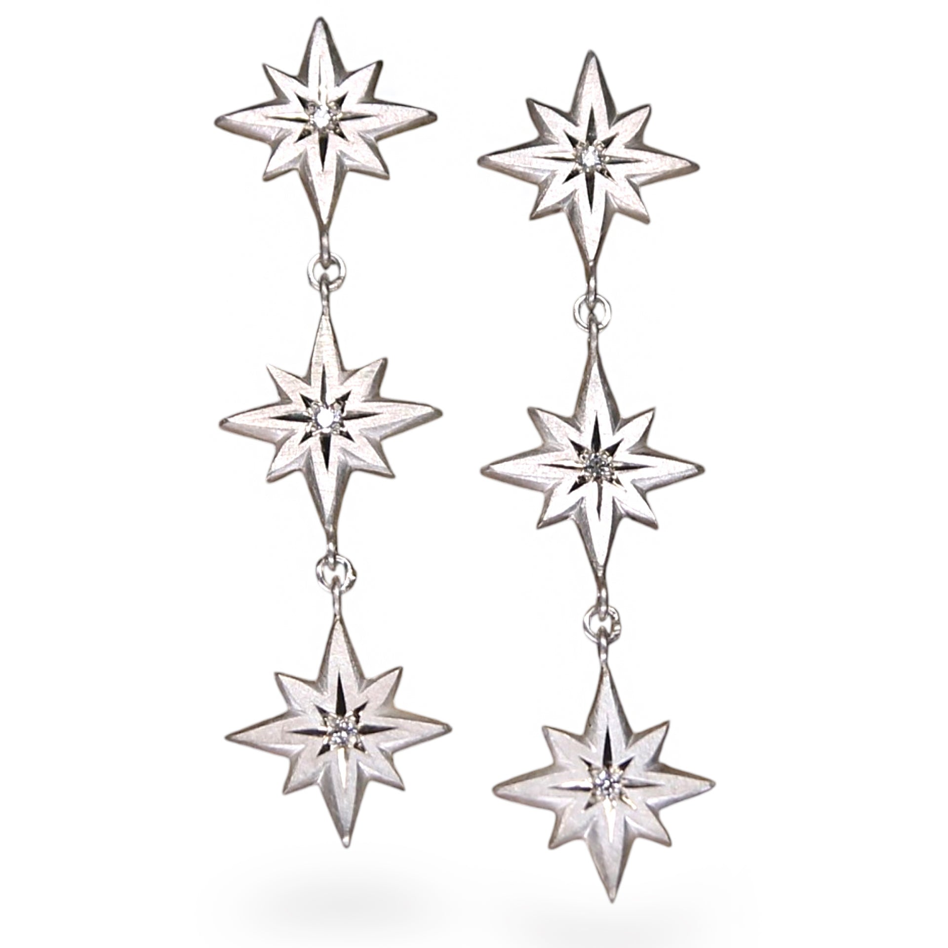 A pair of silver dangle earrings featuring three stacked starburst motifs with small clear crystal accents, shown against a plain white background.